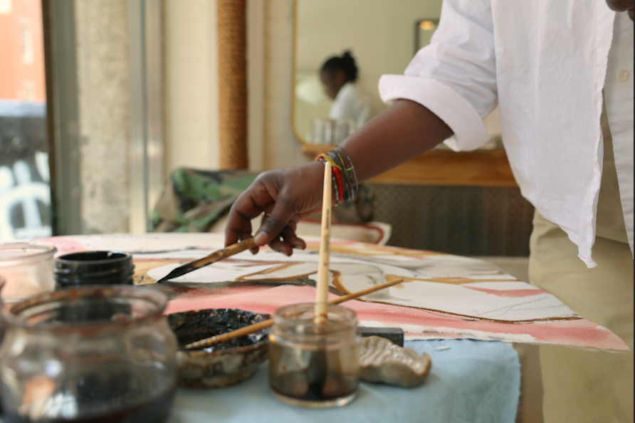 A hand paints with a thin long paint brush. Several jars with paintbrushes are blurred in foreground. 